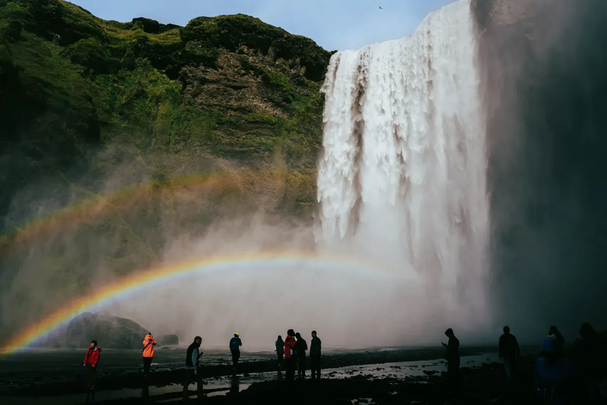 Beautiful view of Skógafoss waterfall in Iceland with a bright rainbow and visitors below.