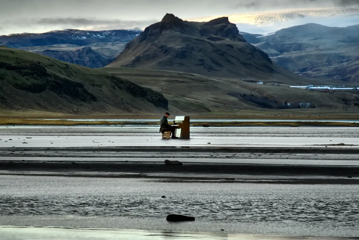 A musician playing piano by a tranquil lake with stunning mountain views in Iceland.